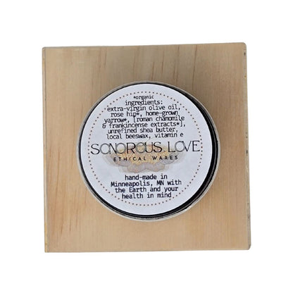 Top view of herbal balm product with 'Sonorous Love' label upon a wooden block