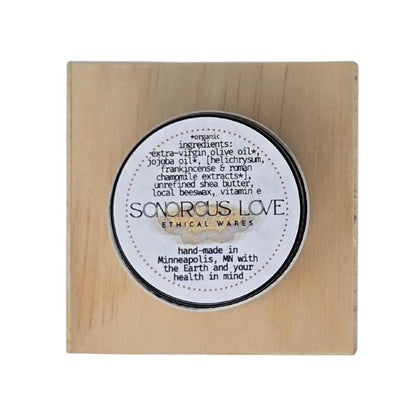 Balm jar top on a wooden box with 'Sonorous Love' branding and ingredients.