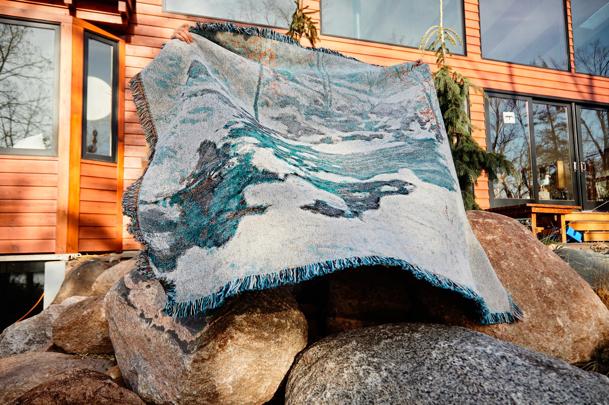 Icebound by John Henry Twachtman, featuring a serene abstract artwork nature scene with curves of ice and snow; white, blue and orange leaves. eco-friendly cotton woven blanket. Person holding up blanket over a white background. Person holding blanket up while standing on rocks in front of a home.